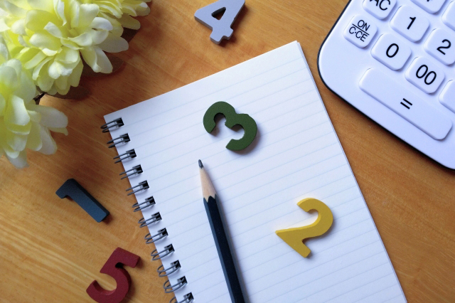 鉛筆が乗っているノートと電卓とお花と散らばっている1~5までの数字の画像